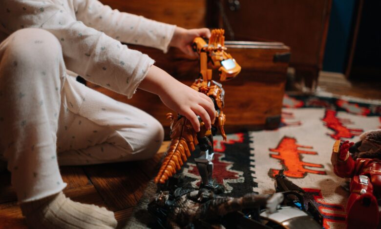 A child in pajamas plays with a toy dinosaur on a colorful rug indoors.