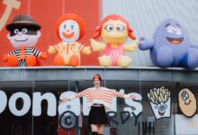 Woman posing happily in front of colorful inflatable fast food characters, radiating playful energy.