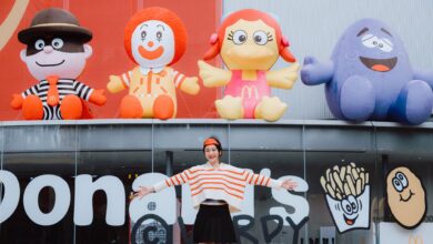 Woman posing happily in front of colorful inflatable fast food characters, radiating playful energy.