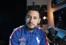 A young male vlogger in a home studio setup with a microphone and computer screen.