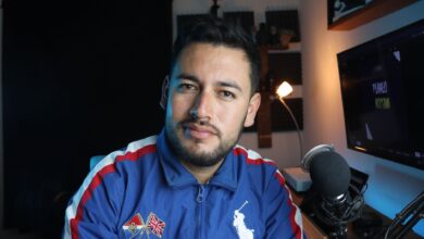 A young male vlogger in a home studio setup with a microphone and computer screen.