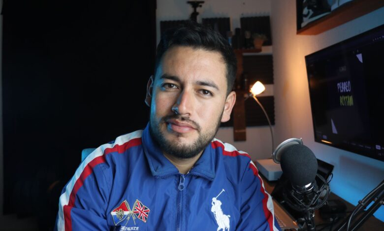 A young male vlogger in a home studio setup with a microphone and computer screen.
