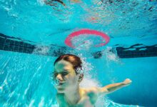 A child energetically plays underwater in a swimming pool, surrounded by bubbles and splashes.