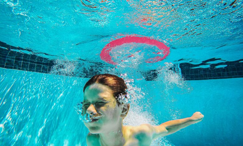 A child energetically plays underwater in a swimming pool, surrounded by bubbles and splashes.