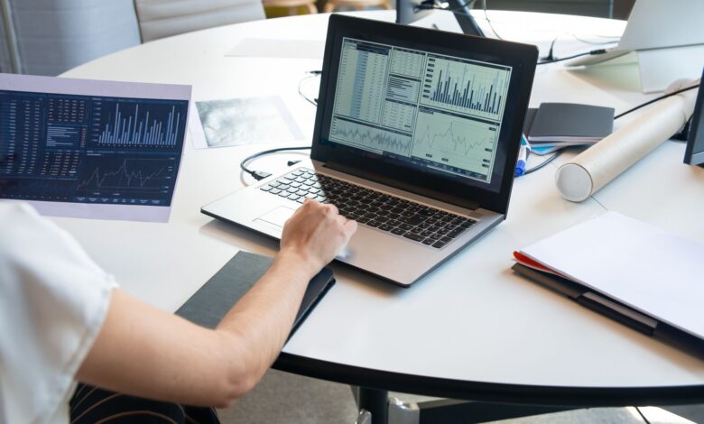 Business person evaluating financial charts on a laptop in a modern office setting.