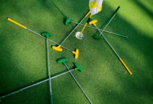 Top view of colorful putters scattered around a golf hole on lush green grass.