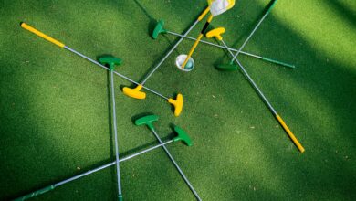 Top view of colorful putters scattered around a golf hole on lush green grass.