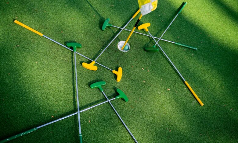 Top view of colorful putters scattered around a golf hole on lush green grass.