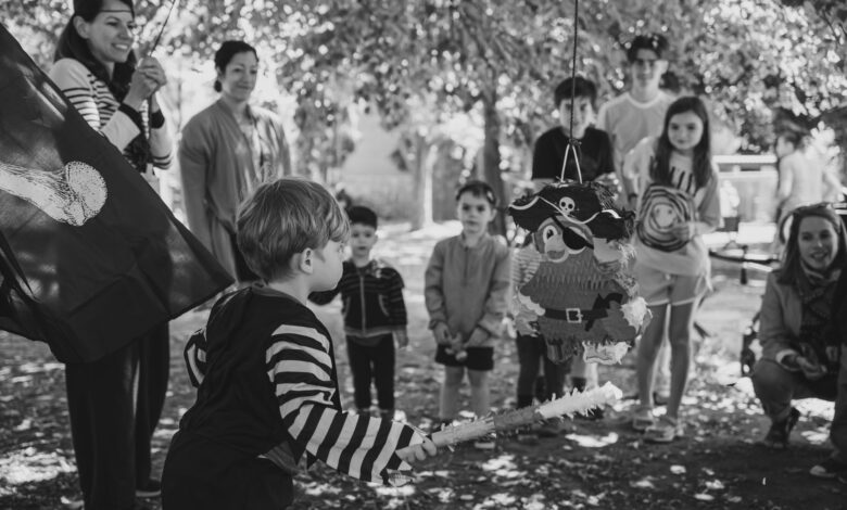 Children at a pirate-themed birthday party outdoors, ready to hit the piñata.