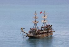 A historic pirate ship sails in clear waters under a sunny sky, adorned with a Turkish flag.