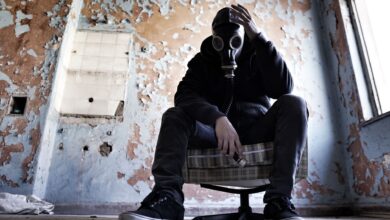 A man wearing a gas mask is seated in a dilapidated room, conveying a sense of despair and survival.