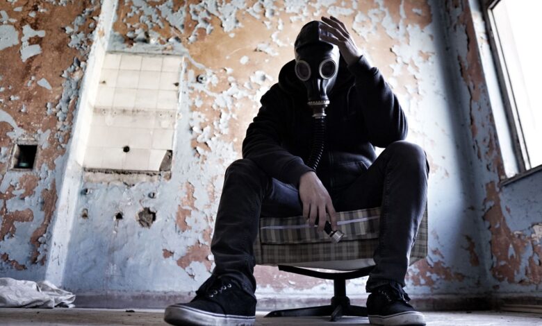 A man wearing a gas mask is seated in a dilapidated room, conveying a sense of despair and survival.