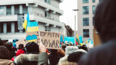 Peaceful protest in an urban setting featuring anti-war signage and Ukrainian flags.