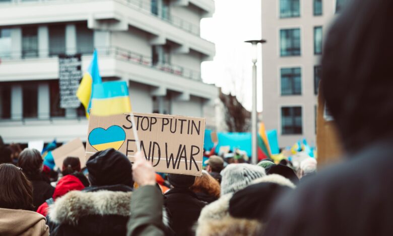 Peaceful protest in an urban setting featuring anti-war signage and Ukrainian flags.
