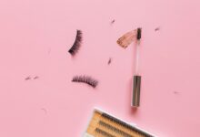 Styled flat lay of false eyelashes and makeup brush on a pastel pink surface.