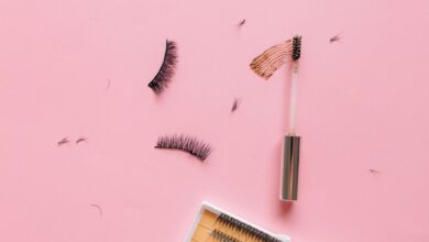 Styled flat lay of false eyelashes and makeup brush on a pastel pink surface.