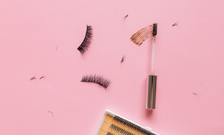 Styled flat lay of false eyelashes and makeup brush on a pastel pink surface.