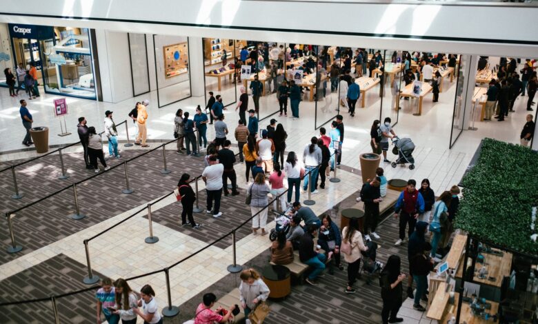 A bustling shopping center with a large crowd queuing inside an Apple Store.