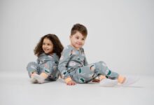Two happy children sitting and smiling in matching pajamas with a white background.