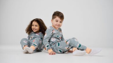 Two happy children sitting and smiling in matching pajamas with a white background.