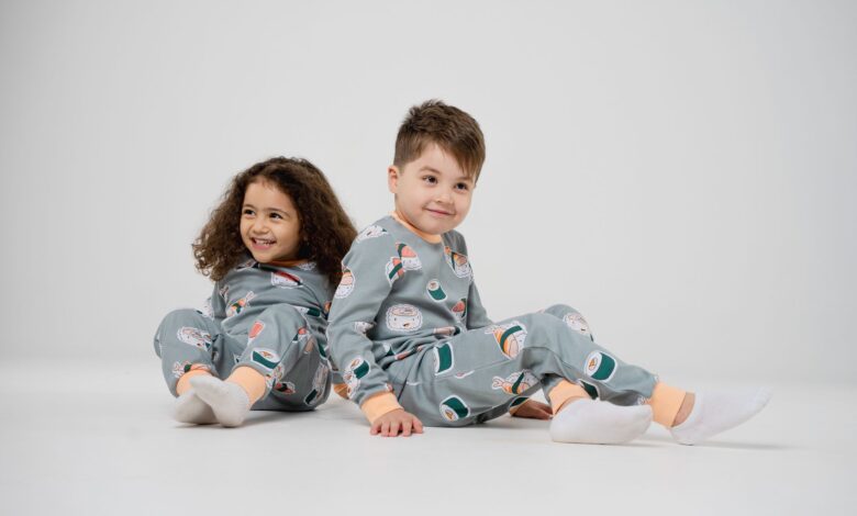 Two happy children sitting and smiling in matching pajamas with a white background.