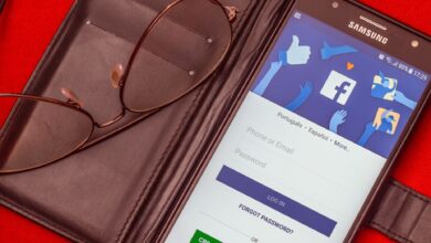 Close-up of a smartphone displaying a Facebook login screen next to eyeglasses on a red background.