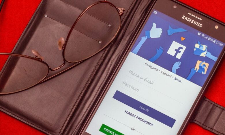 Close-up of a smartphone displaying a Facebook login screen next to eyeglasses on a red background.