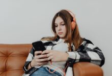 Teenage girl sitting on a sofa listening to music on headphones and using a smartphone.