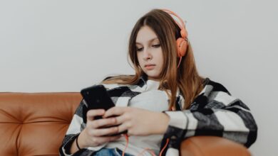 Teenage girl sitting on a sofa listening to music on headphones and using a smartphone.