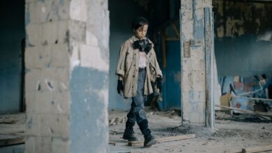A young child walks in a post-apocalyptic, abandoned building wearing a gas mask.