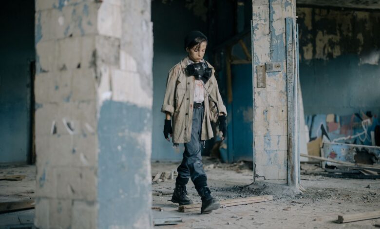 A young child walks in a post-apocalyptic, abandoned building wearing a gas mask.