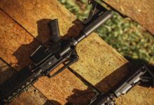 AR-style rifle displayed on wooden planks in natural light, showcasing tactical features.