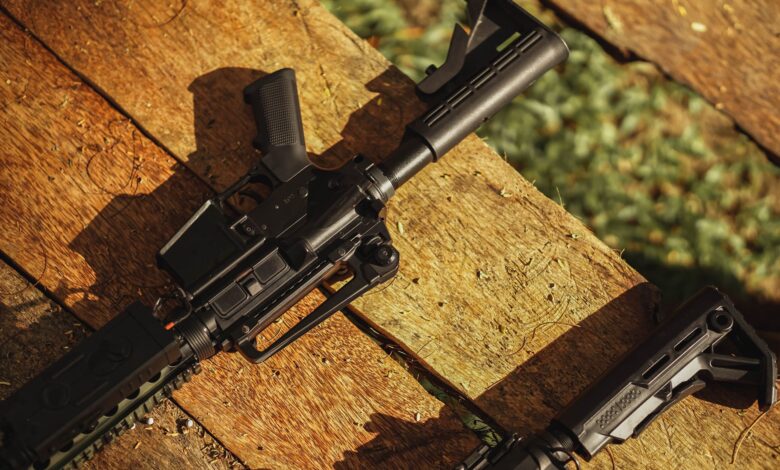 AR-style rifle displayed on wooden planks in natural light, showcasing tactical features.