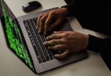 From above of crop anonymous male hacker typing on netbook with data on screen while sitting at desk