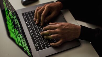 From above of crop anonymous male hacker typing on netbook with data on screen while sitting at desk