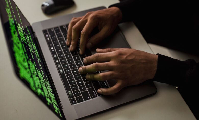 From above of crop anonymous male hacker typing on netbook with data on screen while sitting at desk