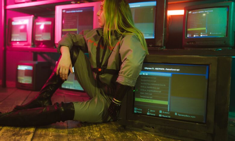 Woman in cyberpunk attire sits surrounded by vintage TVs in a neon-lit room, evoking retro-futuristic vibes.