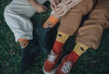 Two friends wearing playful socks sit closely on grass, showing comfort and friendship.