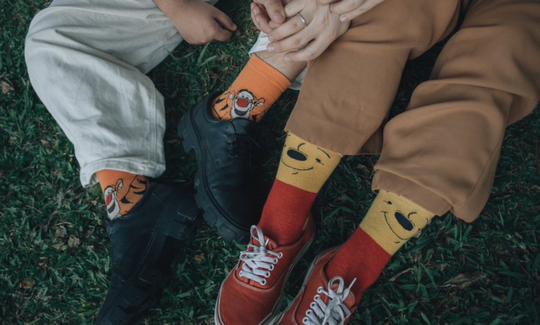 Two friends wearing playful socks sit closely on grass, showing comfort and friendship.