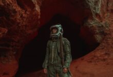 Astronaut in helmet explores a rugged, red-hued cave, exuding adventure and mystery.