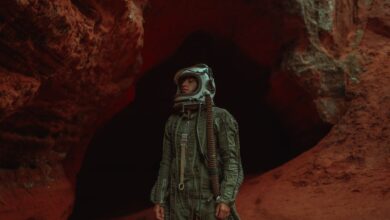 Astronaut in helmet explores a rugged, red-hued cave, exuding adventure and mystery.