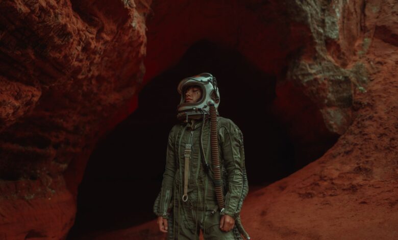 Astronaut in helmet explores a rugged, red-hued cave, exuding adventure and mystery.