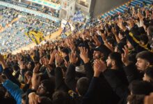 Energetic fans with raised hands in a stadium, supporting their soccer team with enthusiasm.
