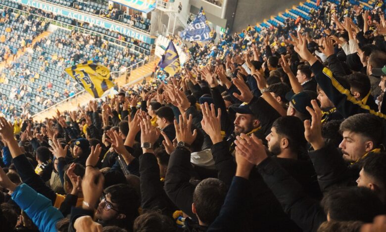 Energetic fans with raised hands in a stadium, supporting their soccer team with enthusiasm.