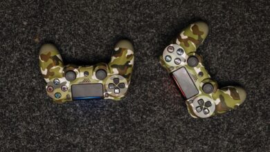 Two camouflage-patterned game controllers displayed on a textured, dark surface from above.
