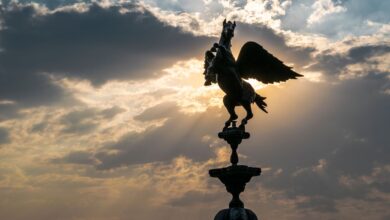 A stunning silhouette of a Pegasus sculpture against a dramatic sunset sky with sun rays.