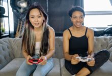 Two women playing video games on a sofa, sharing a fun leisure moment indoors.