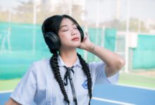 Asian girl in school uniform with braided hair listens to music outdoors.