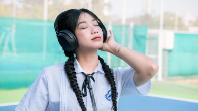 Asian girl in school uniform with braided hair listens to music outdoors.