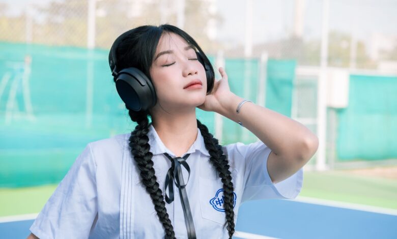 Asian girl in school uniform with braided hair listens to music outdoors.